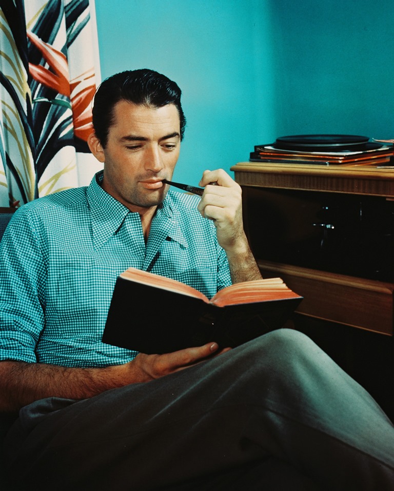 Gregory Peck, une pipe à la main, feuillette un livre en écoutant de la musique grâce à un tourne-disque